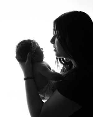 Black and white silhouette of mother tenderly holding newborn baby up to her face.