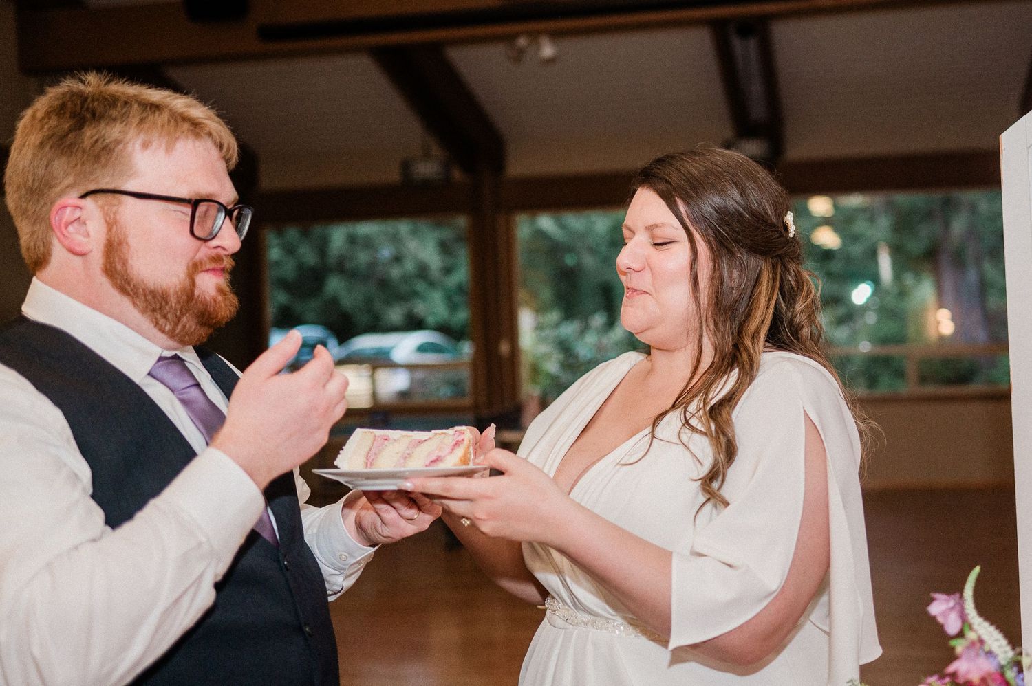 Bride and groom share their first bite of wedding cake during an intimate indoor reception celebration.