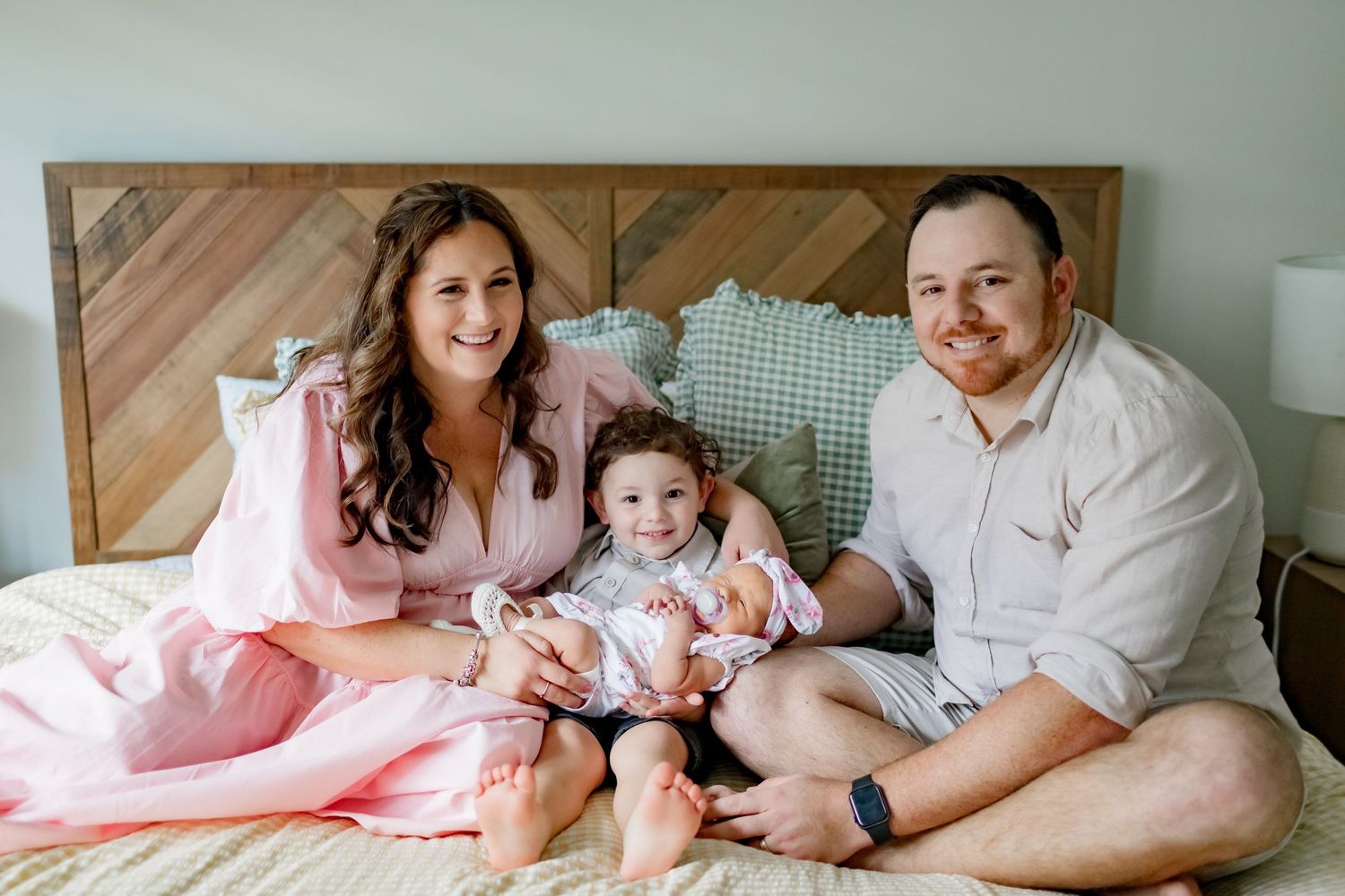 A family relaxes together on a bed with a chevron wood headboard.