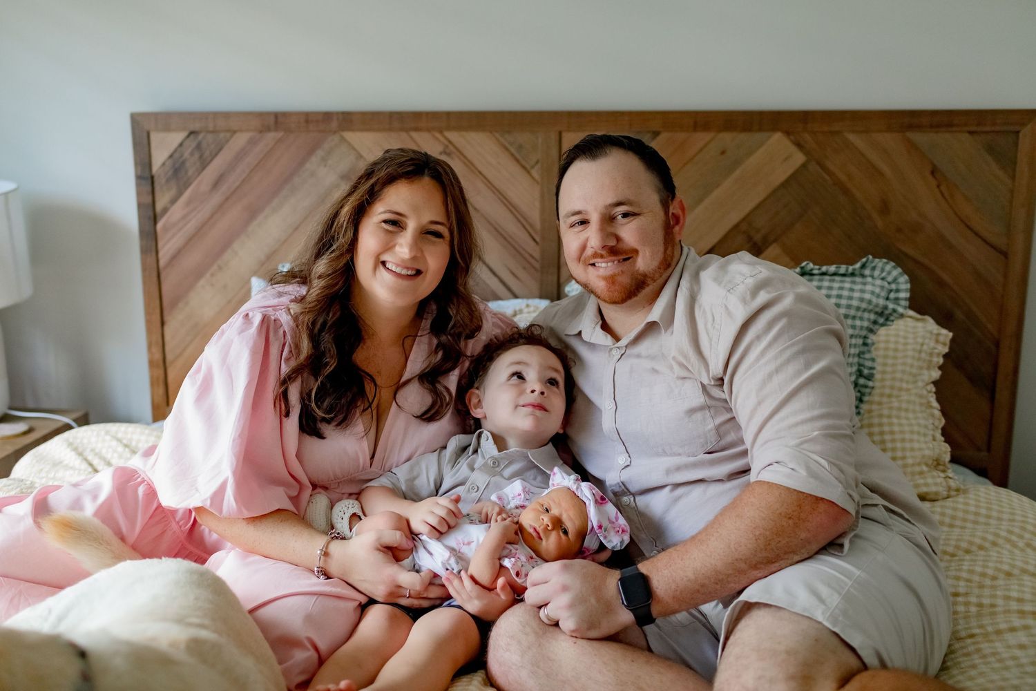 A relaxed family portrait on a bed with geometric wooden headboard.