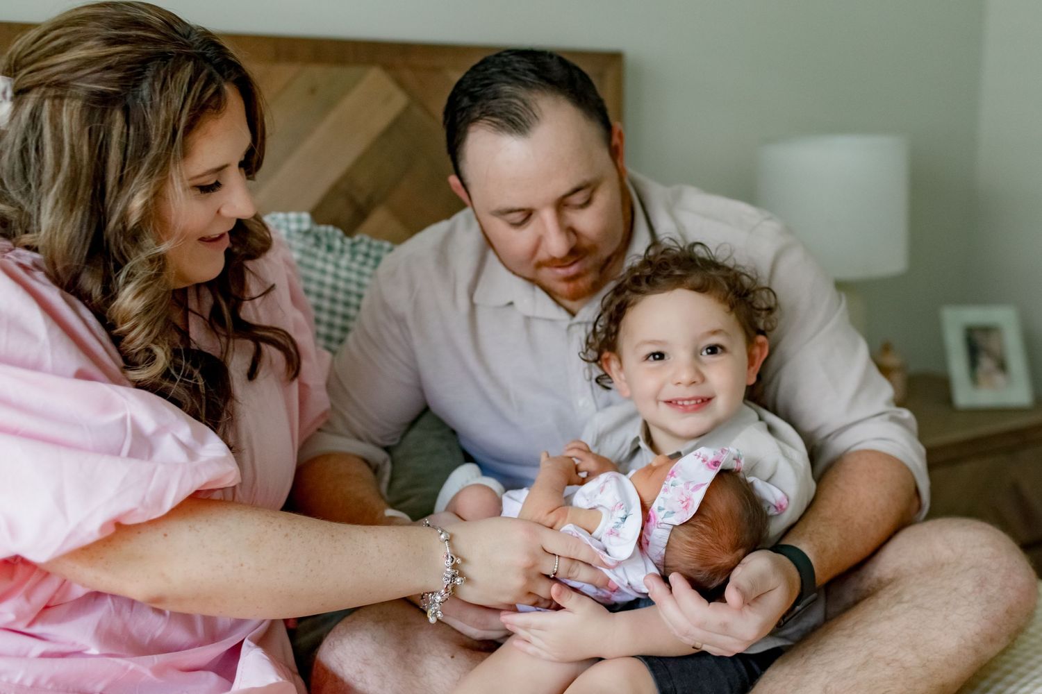 A tender family moment shared on a bed with a newborn baby and floral bedding in natural light.