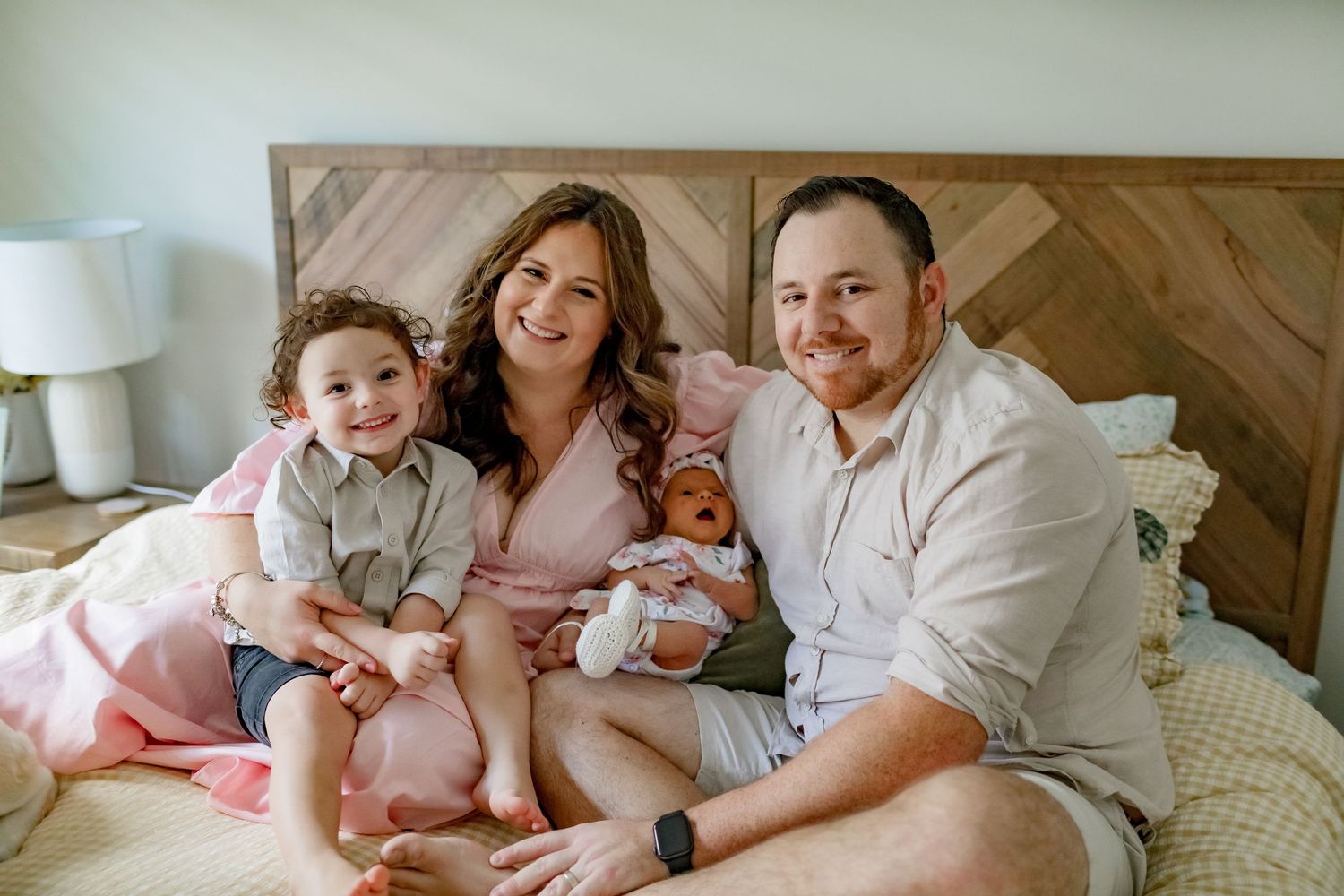 A family of four relaxes together on a bed with chevron headboard and pink accents.