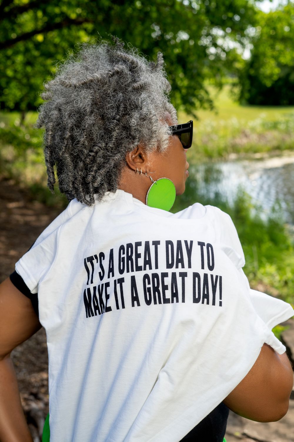 Back view of t-shirt with inspirational quote shown against serene waterfront park setting.
