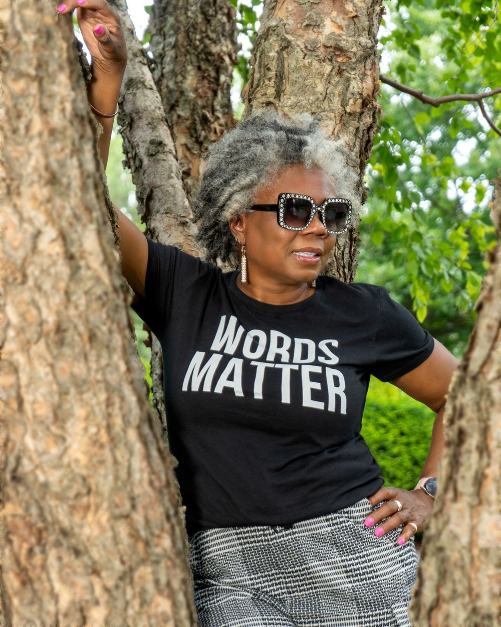 Person wearing 'Words Matter' t-shirt poses against a tree trunk in a natural setting.