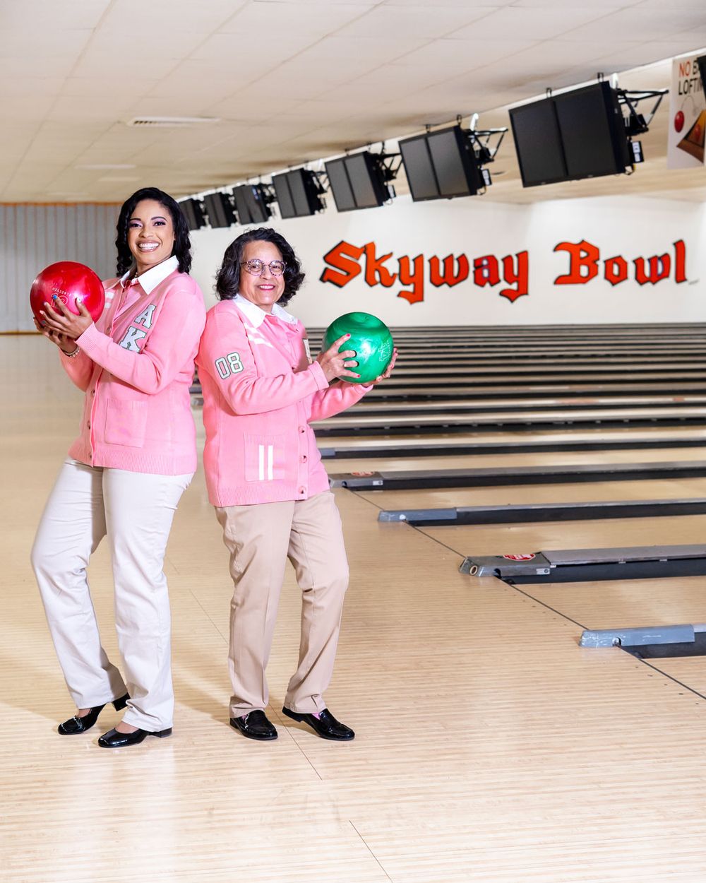 Two bowlers in coordinating pink jackets pose with colorful bowling balls at Skyway Bowl.