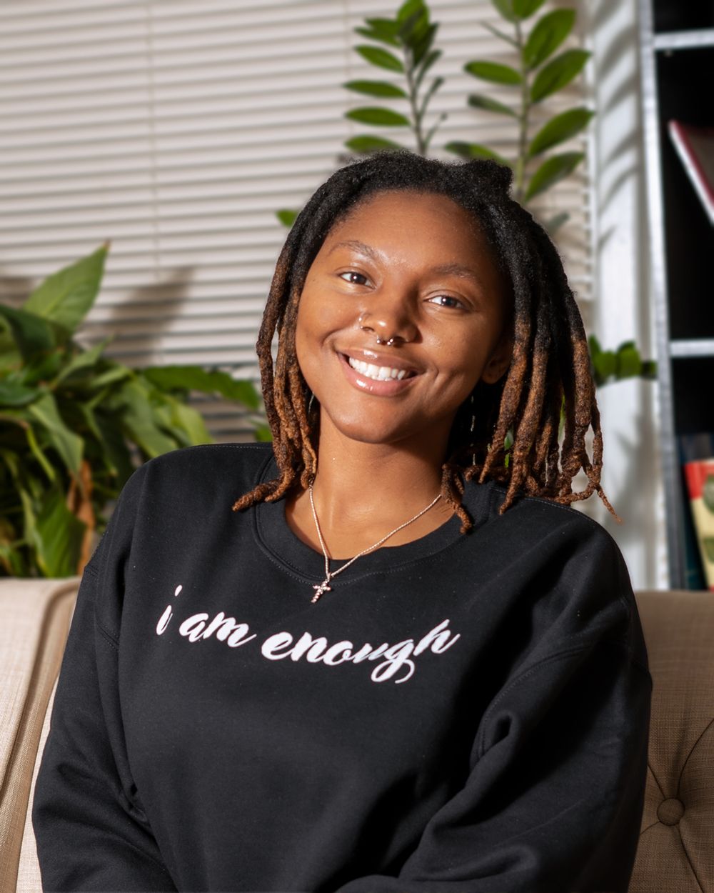 Black sweatshirt with 'I am enough' text shown in cozy home setting with plants.