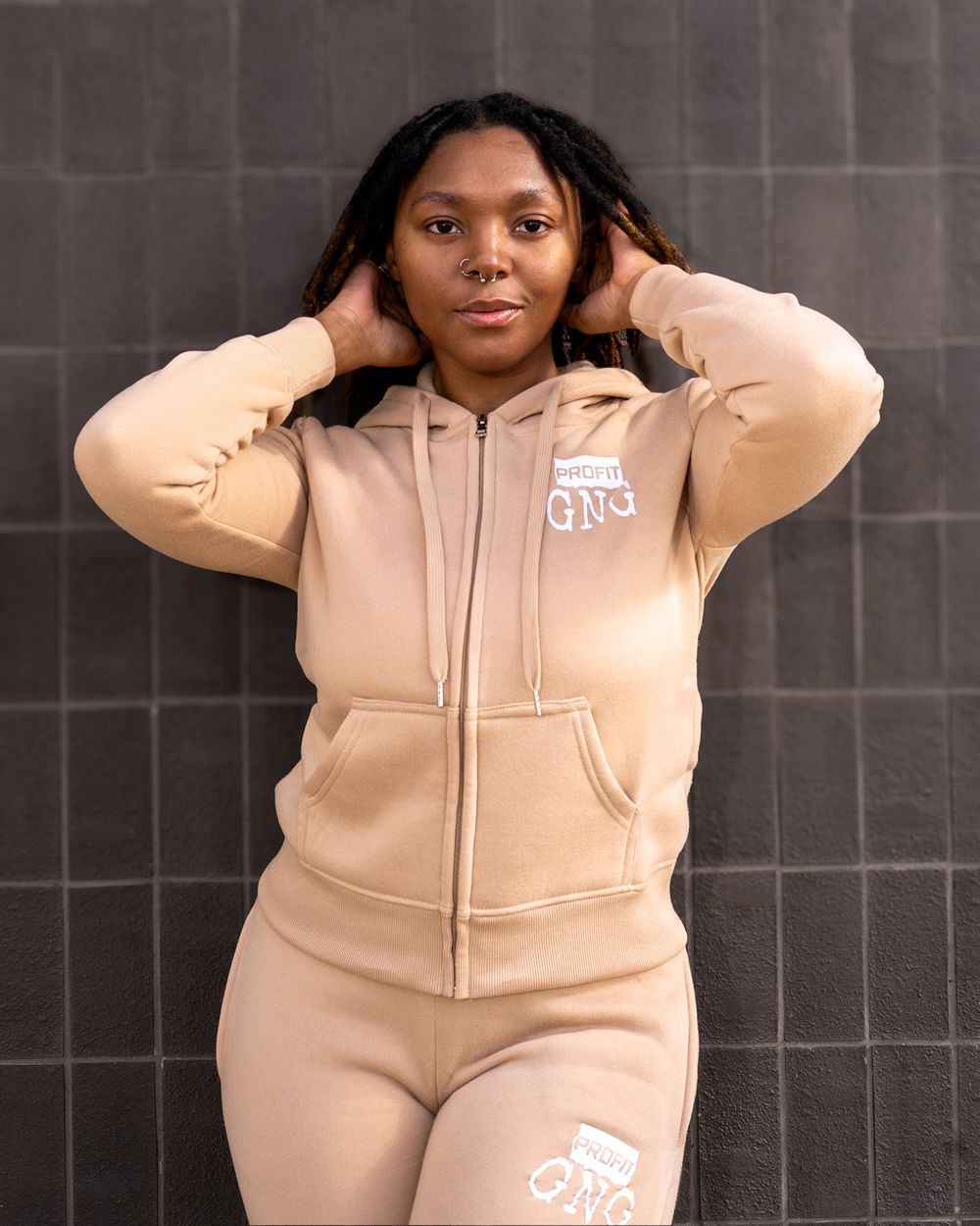 Casual beige tracksuit with white logo shown against dark tile background.