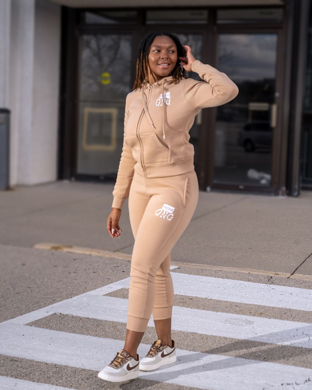 Athletic wear ensemble in nude beige color shown on crosswalk with matching sneakers.