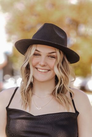 girl in a black hat smiles with fall colors behind her