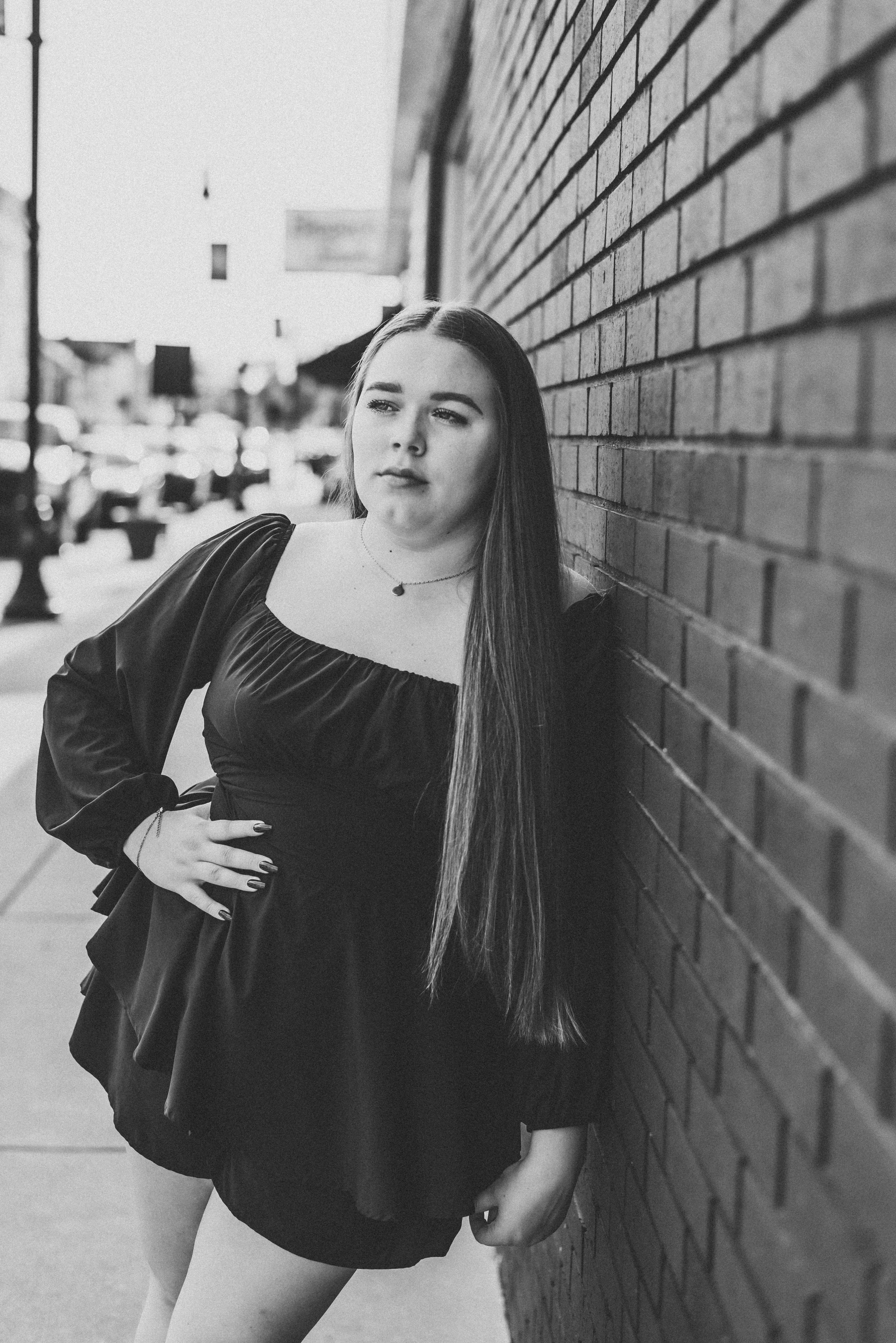 girl in black dress leaning again brick wall