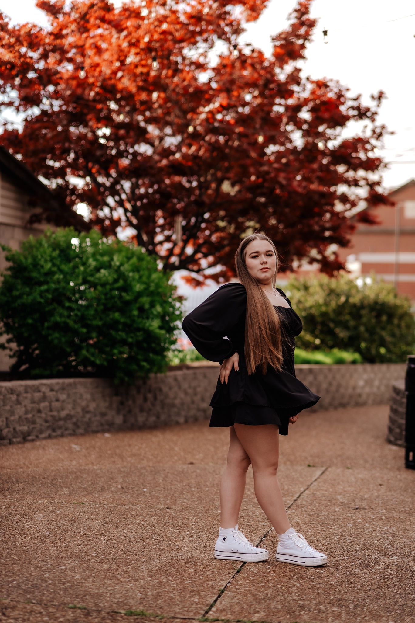 girl in black dress with white sneakers, stands in courtyard
