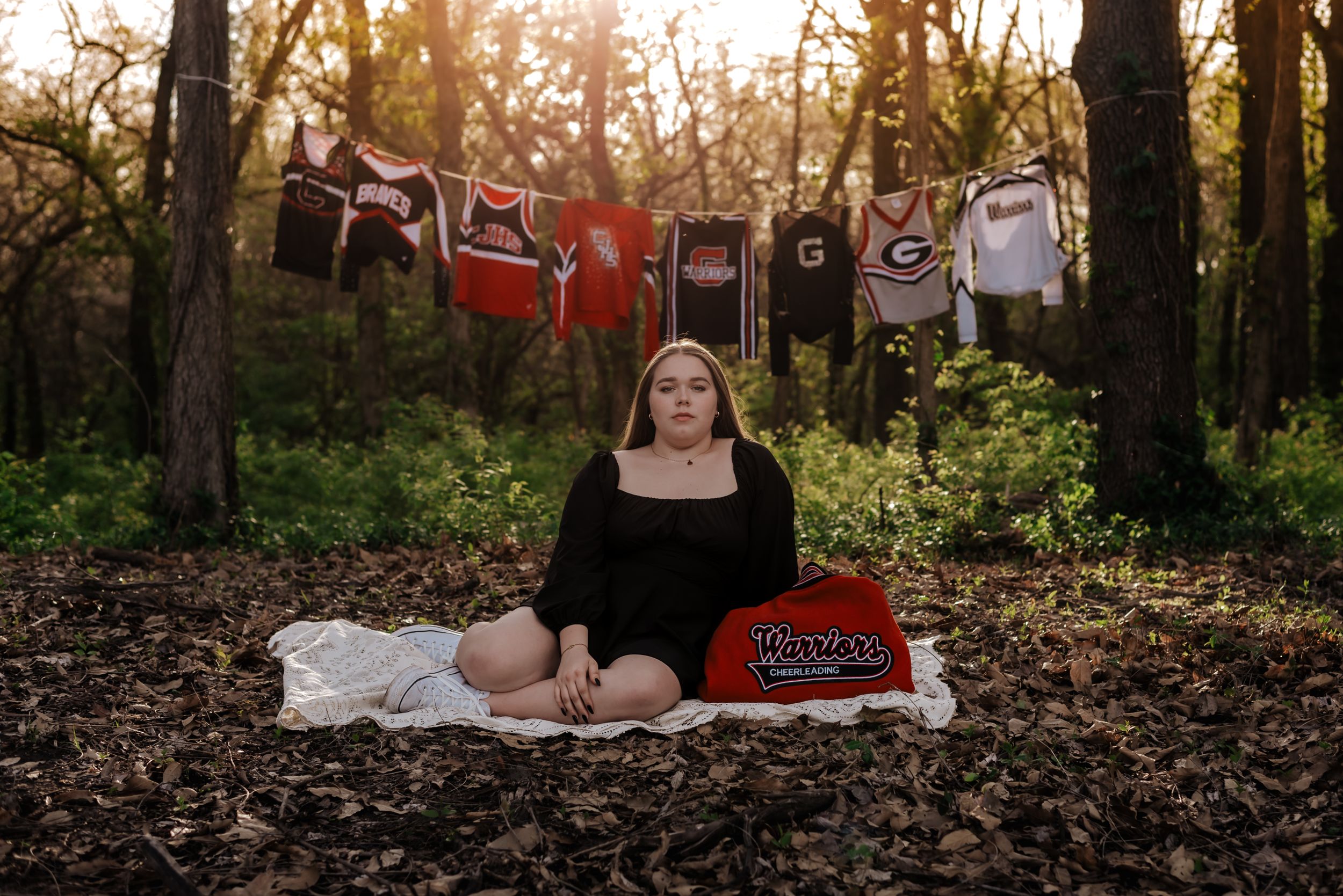 girl sits in front of dance uniforms hanging on clothes line, unsmiling.