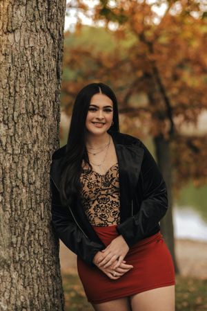 teen girl standing near a tree, with fall colors behind her
