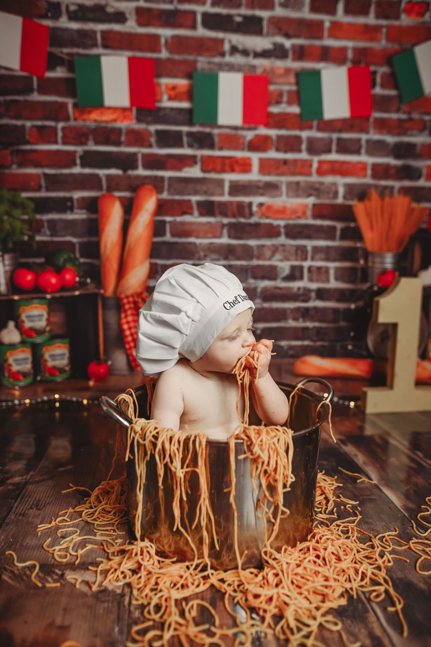 Chef's hat and pasta noodles scattered on a rustic wooden table with brick wall background.