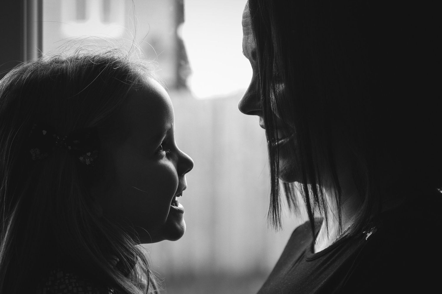 Black and white silhouette of two figures in tender moment against window light.