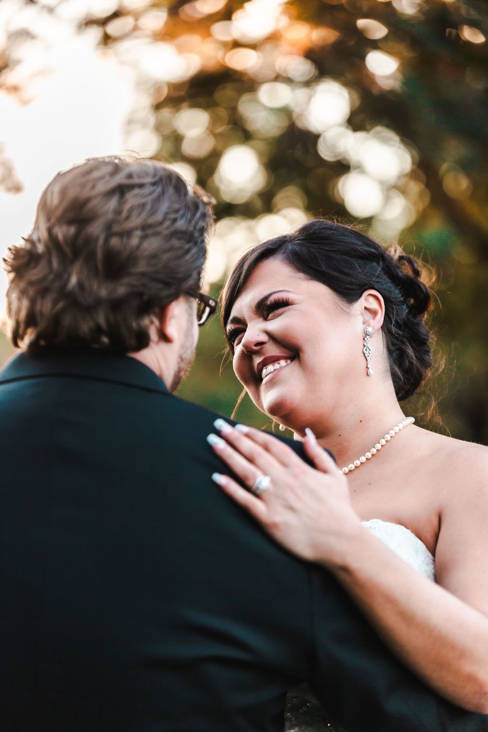 woman wearing a ring in a wedding dress smiling at her husband standing outside