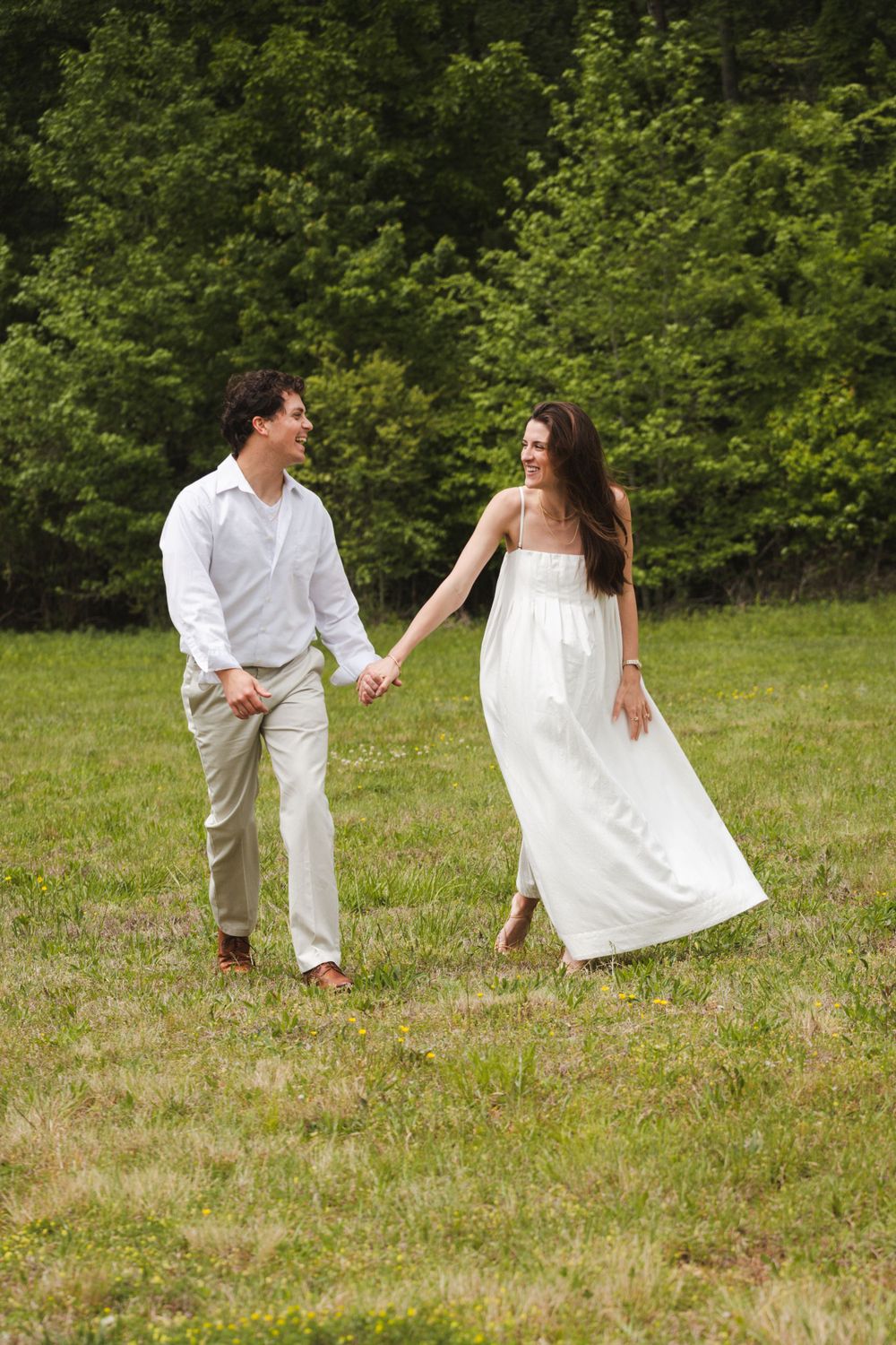 young married couple wearing white holding hands walking outside in a pasture smiling
