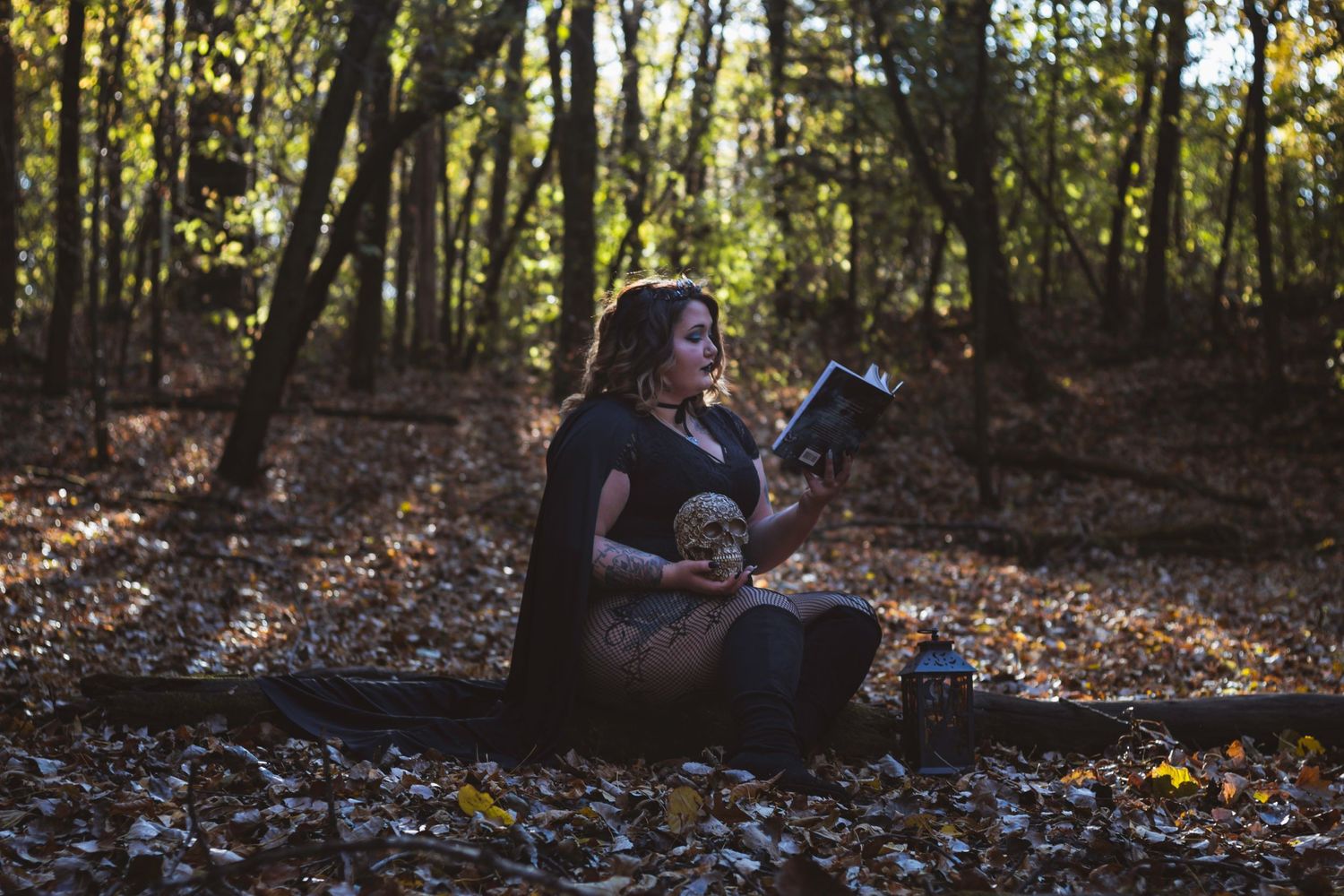 Person sitting among fallen leaves reading in sunlit autumn forest.