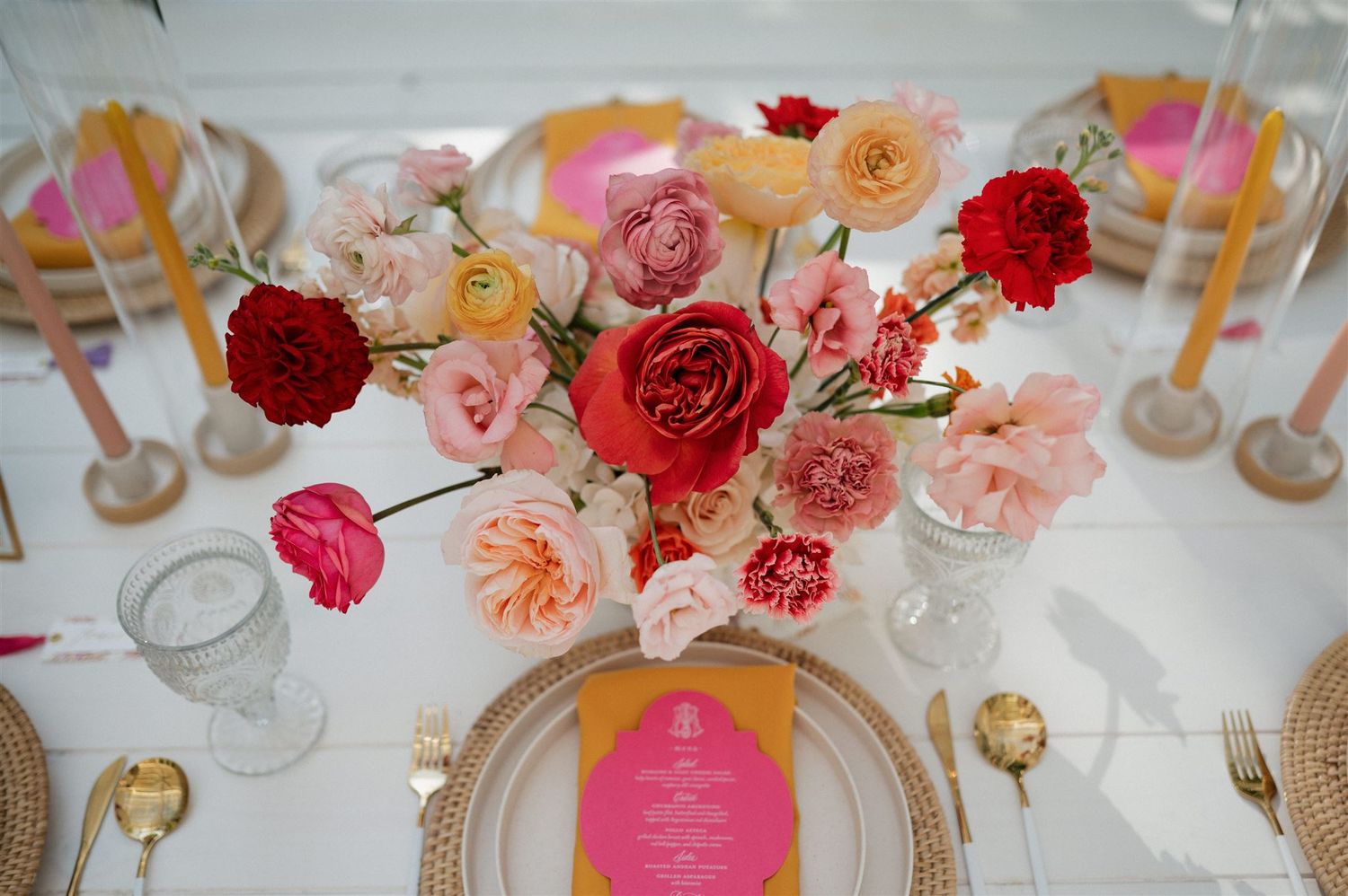 A romantic table setting with pink and coral roses in a centerpiece alongside gold flatware and place settings.