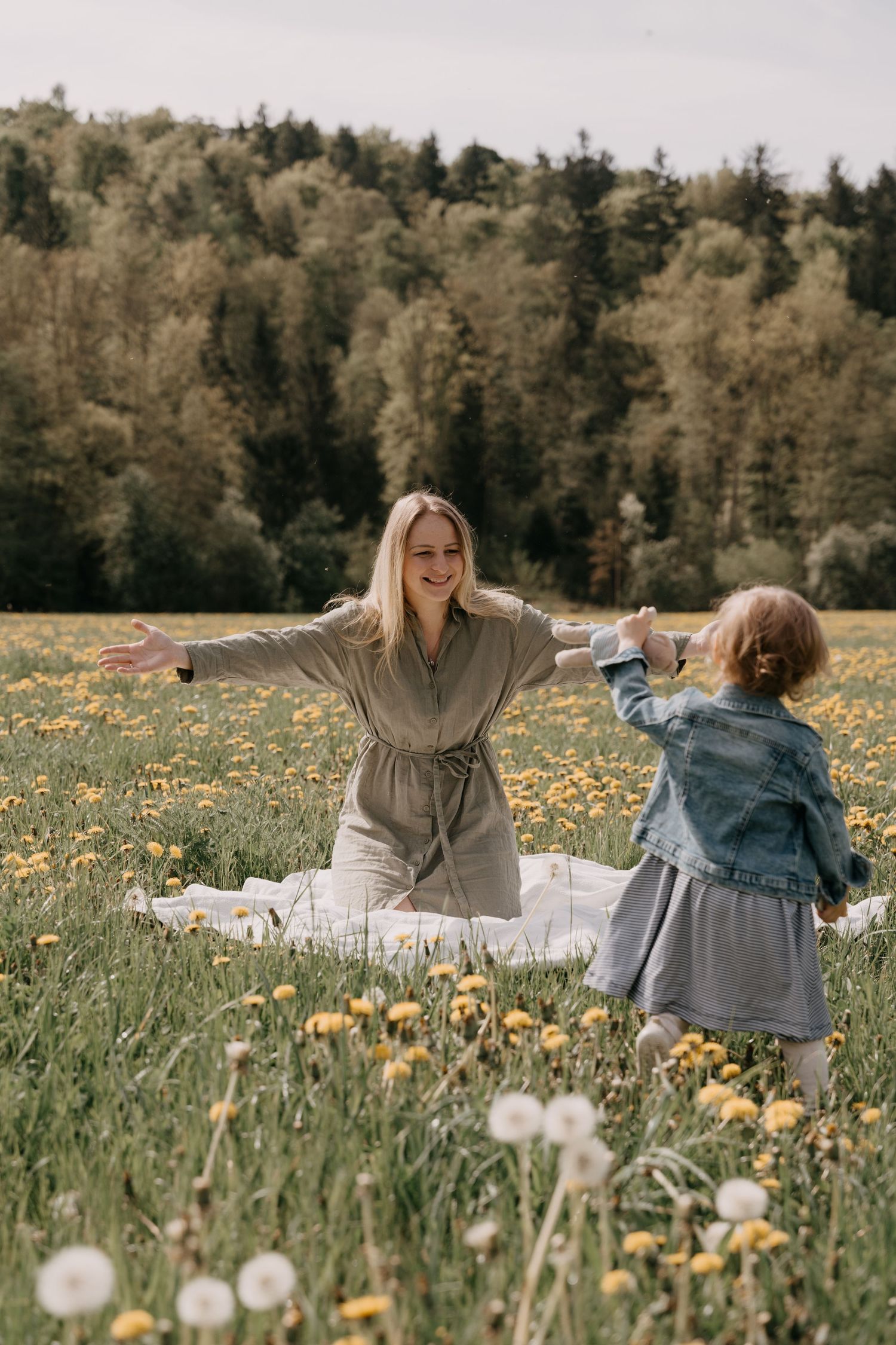A tender moment between parent and child embracing in a wildflower meadow at sunset with forest in background.