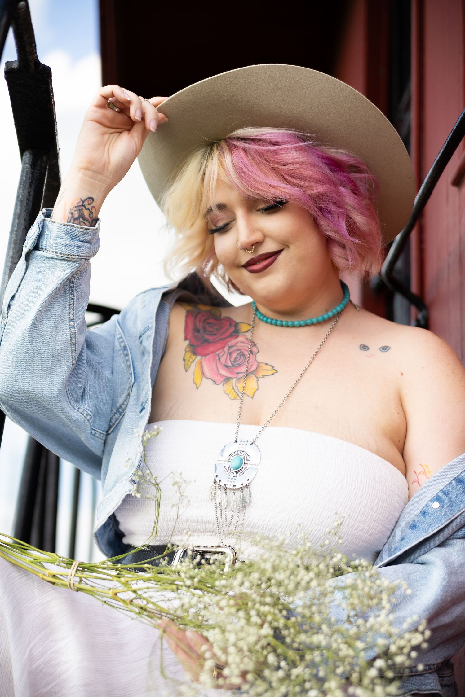 Model in denim with pink hair poses with baby's breath flowers and cowboy hat.