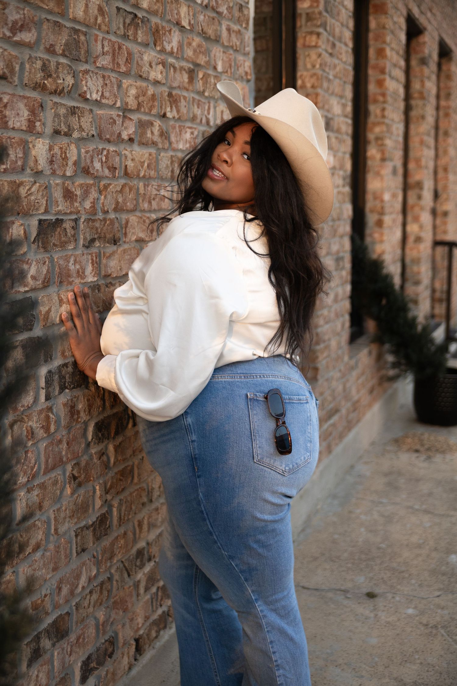 Model in white blouse and jeans strikes dynamic poses against rustic brick backdrop.