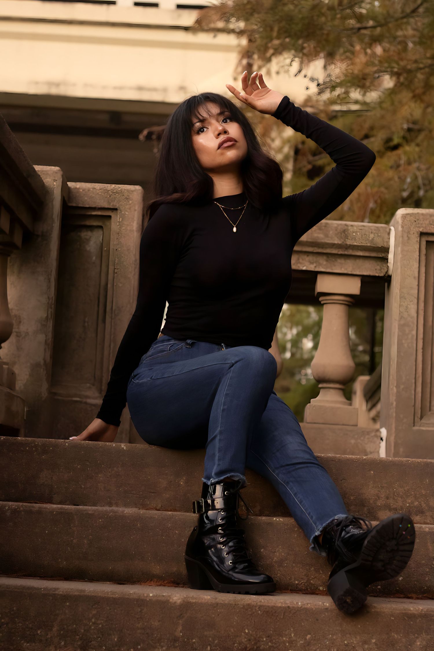 Person in black sweater and jeans poses on stone steps during outdoor photoshoot.