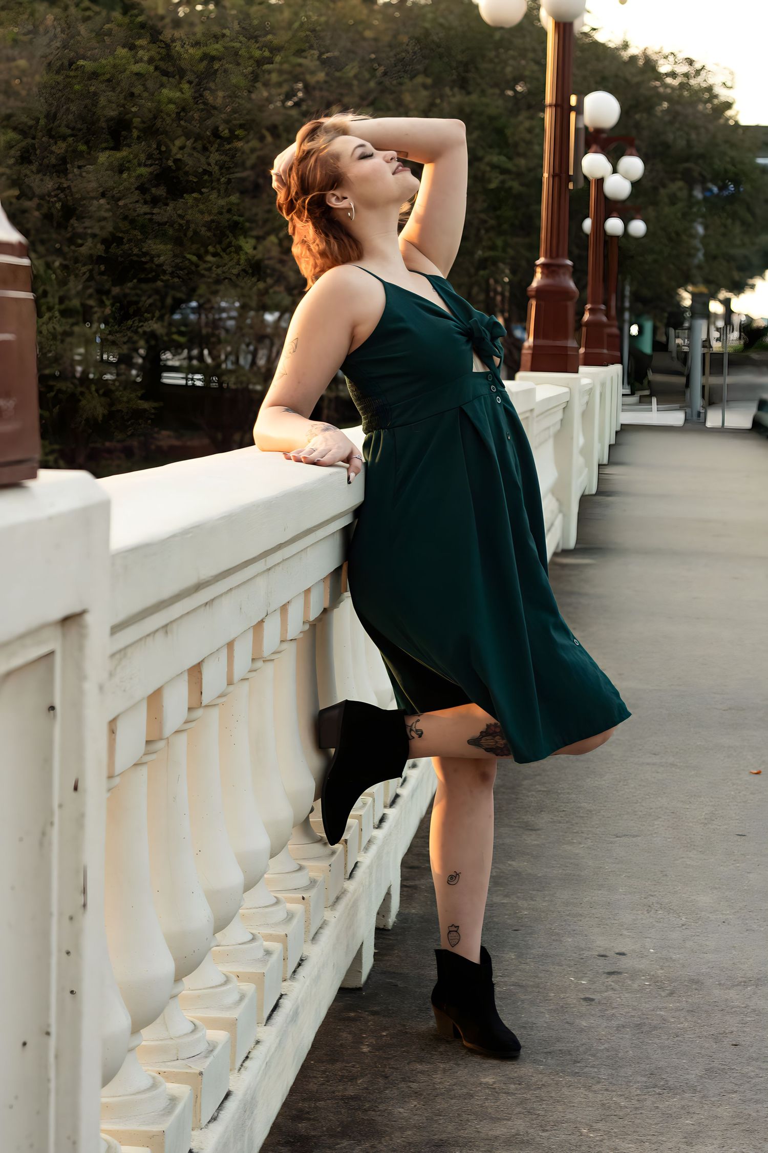 Model in dark dress poses dramatically along white balustrade at sunset.