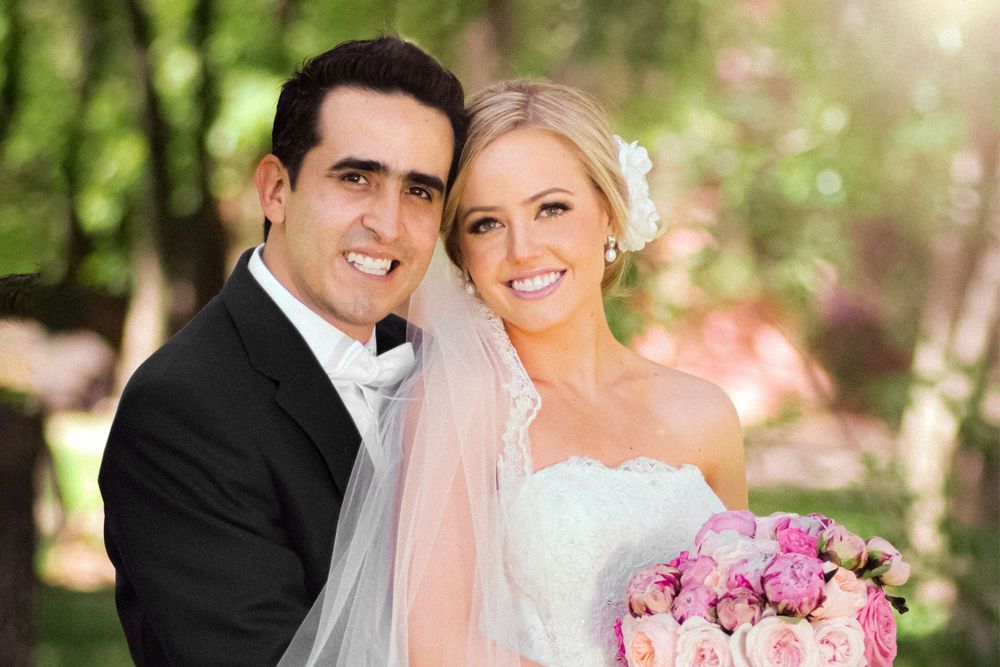 A sunlit outdoor portrait of a couple with pink roses and garden scenery.