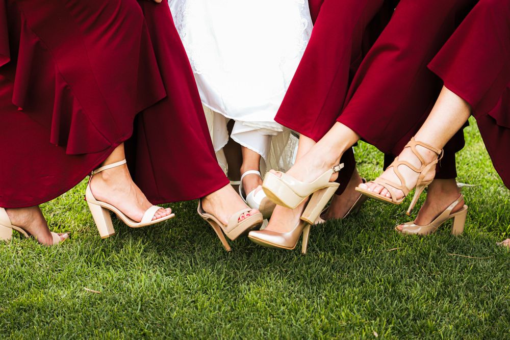 Red-dressed bridesmaids show off their stylish heels while standing together on green grass.