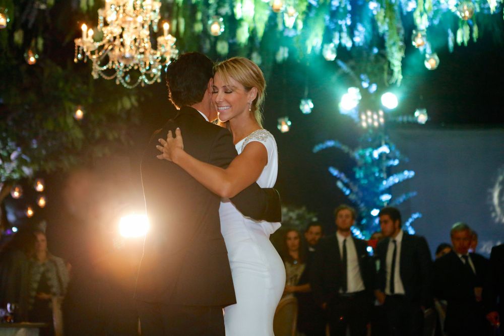 A bride dances under sparkling chandeliers and colored lights at an evening reception.