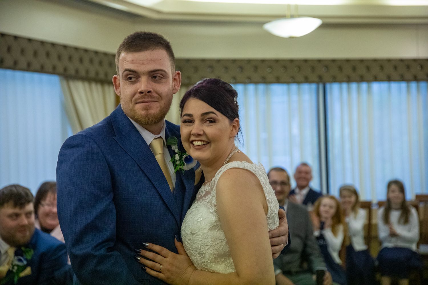 Indoor wedding ceremony portrait in elegant reception hall with chandelier lighting.