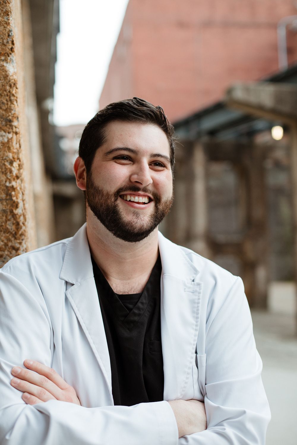 Professional headshot against stone columns wearing white coat and dark shirt.