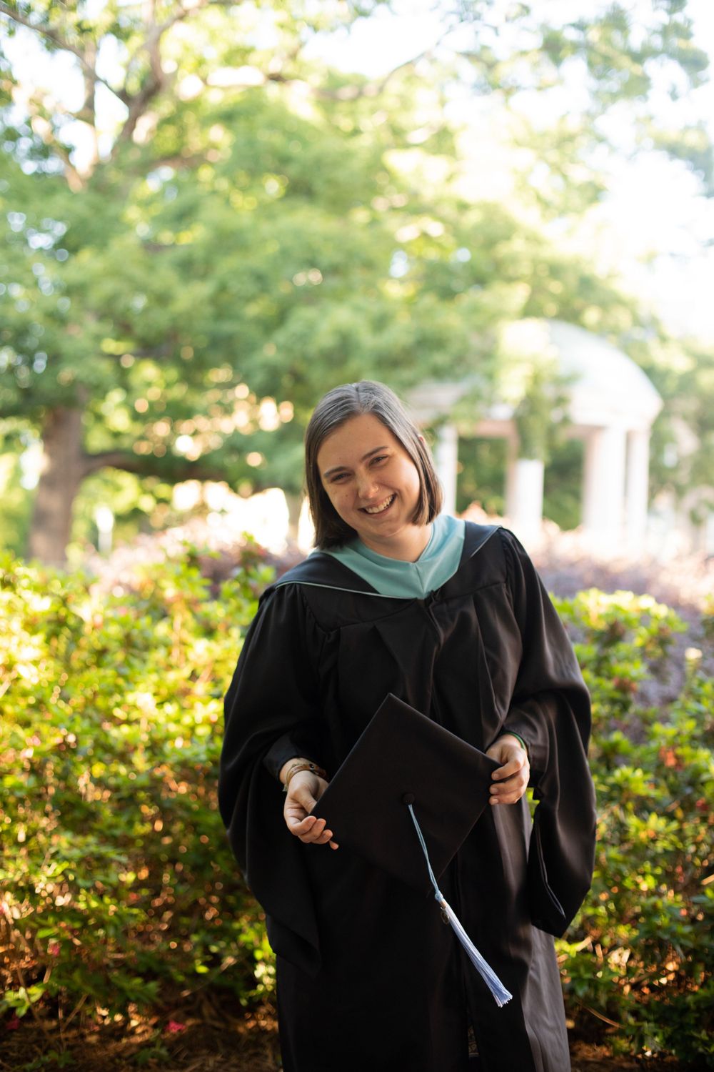 Graduate in black cap and gown laughs joyfully during outdoor photo session.