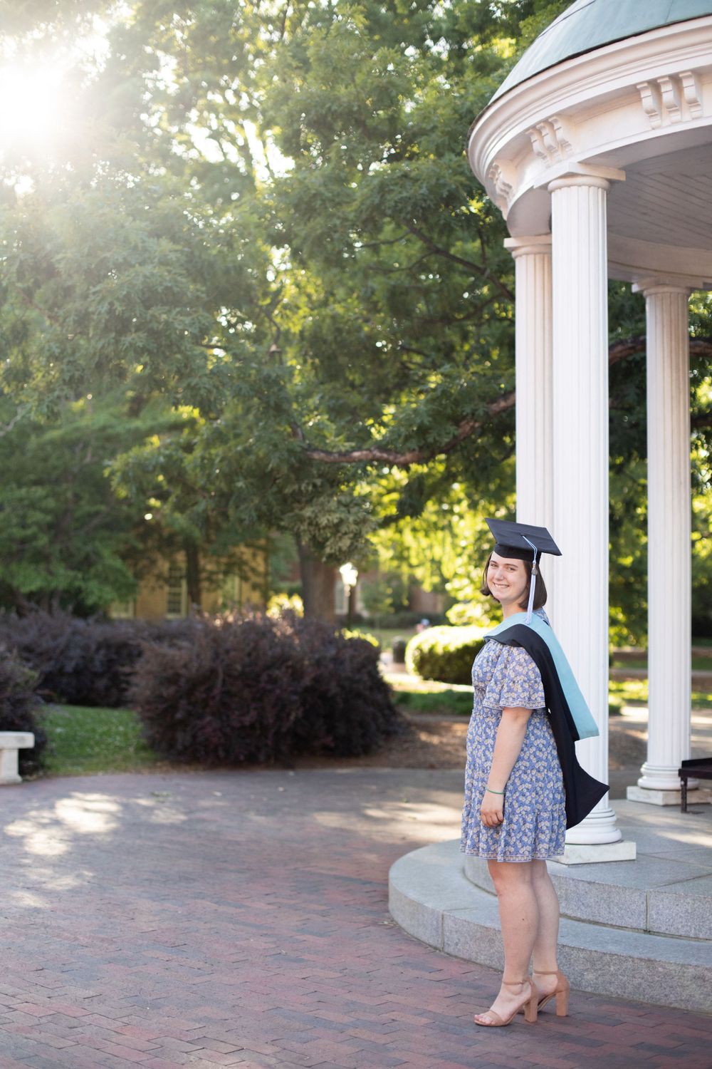 Graduate in floral dress and cap poses near UNC Chapel Hill's old well.