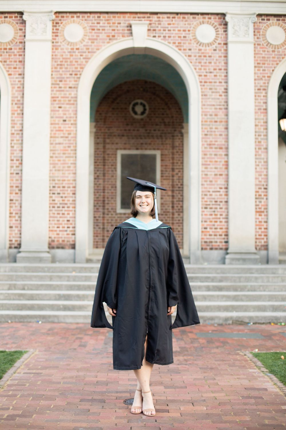 Graduate in academic regalia poses in front of brick and white columned architecture.