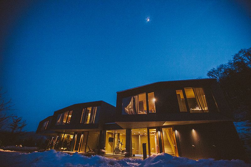 Modern curved architecture home lit from within against dark blue night sky with visible star above.