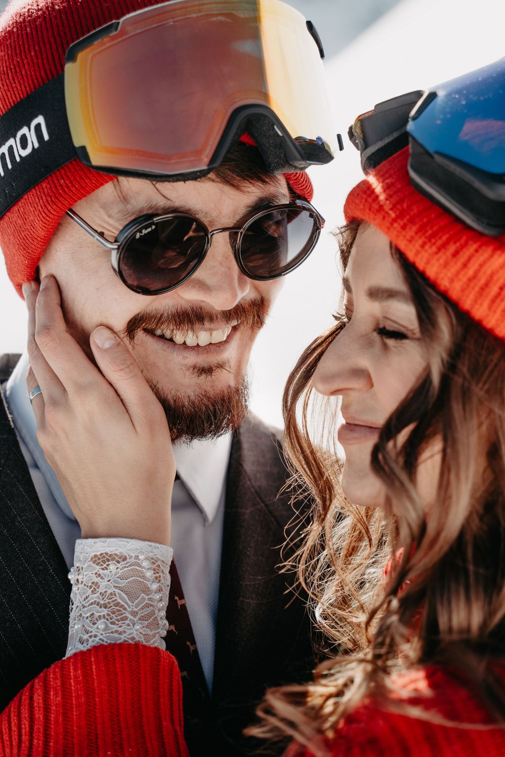Close-up portrait of a man in sunglasses and a woman in a red hat smiling at each other