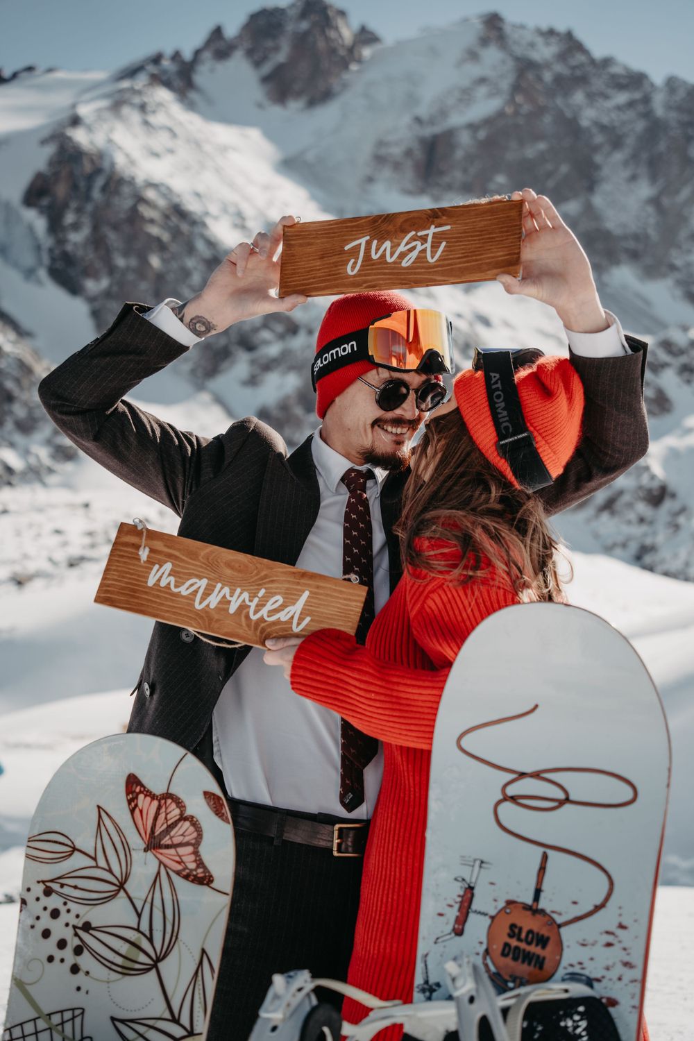Married couple holding 'Just Married' sign and kissing in front of the snowy mountains