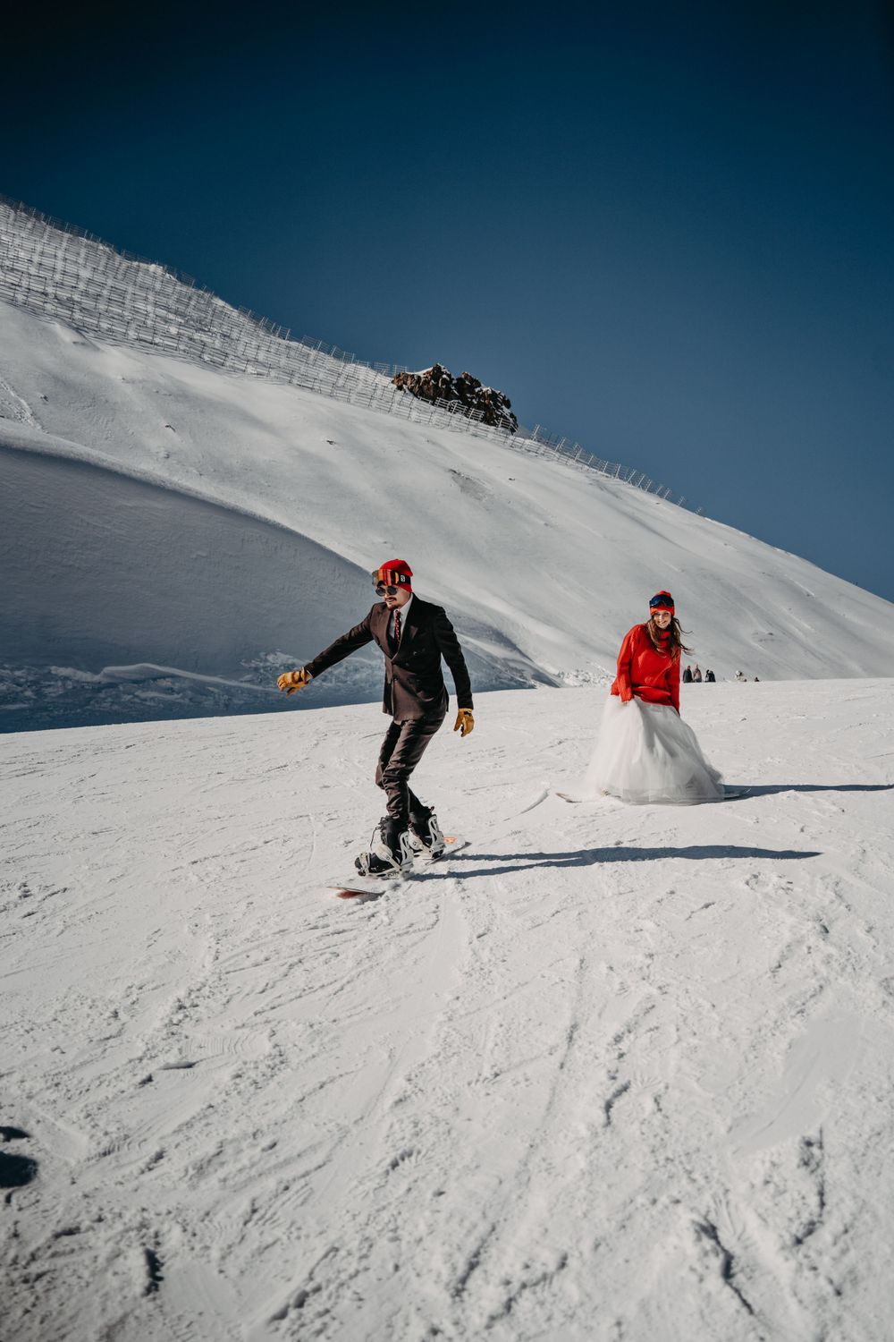 Snowboard-loving couple riding their boards in wedding attire in the snowy mountains