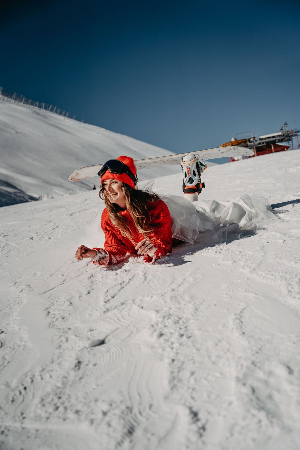 Girl in a wedding dress and red sweater fallen on the snowboard slope