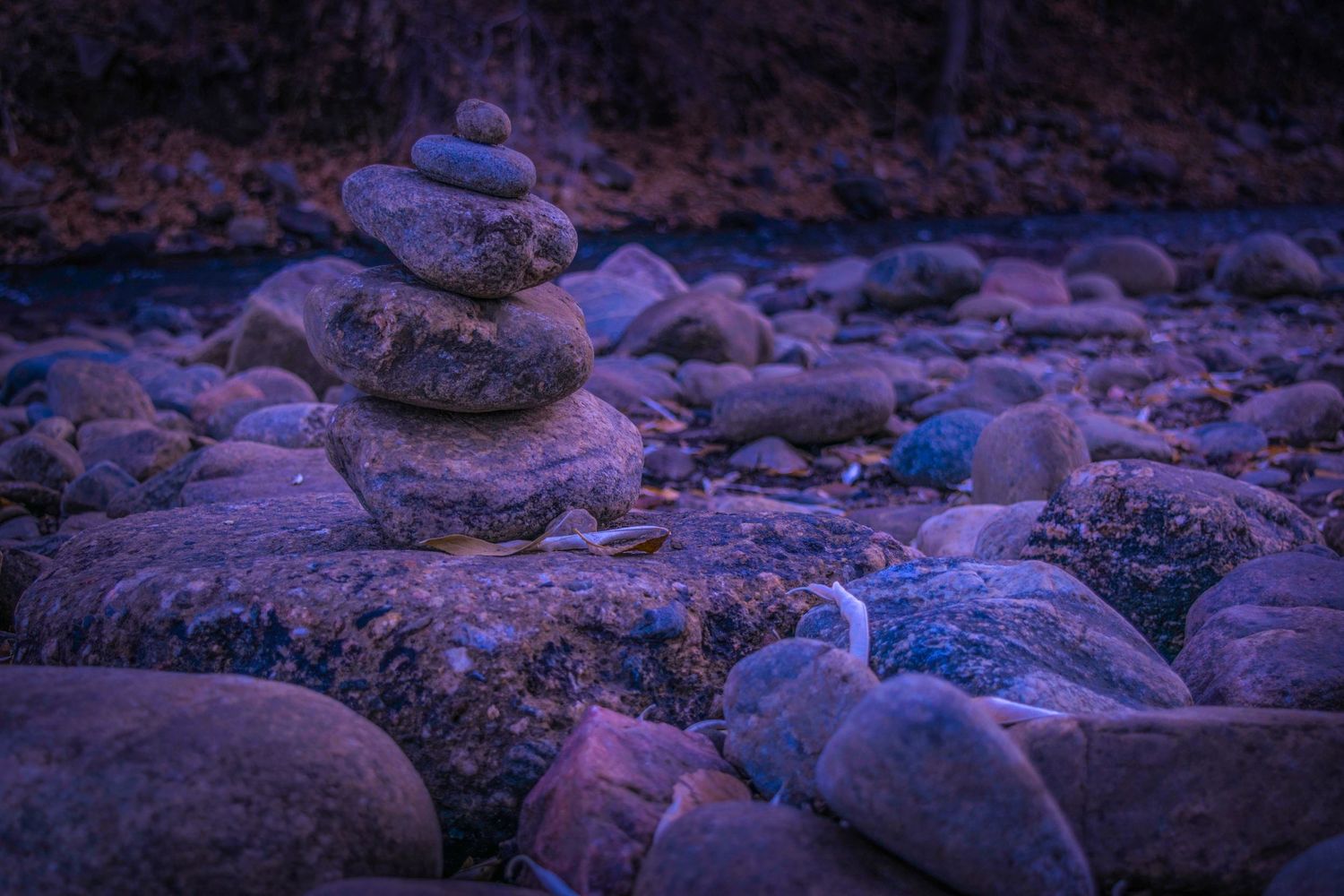 Stone cairn stands among scattered river rocks in purple twilight.