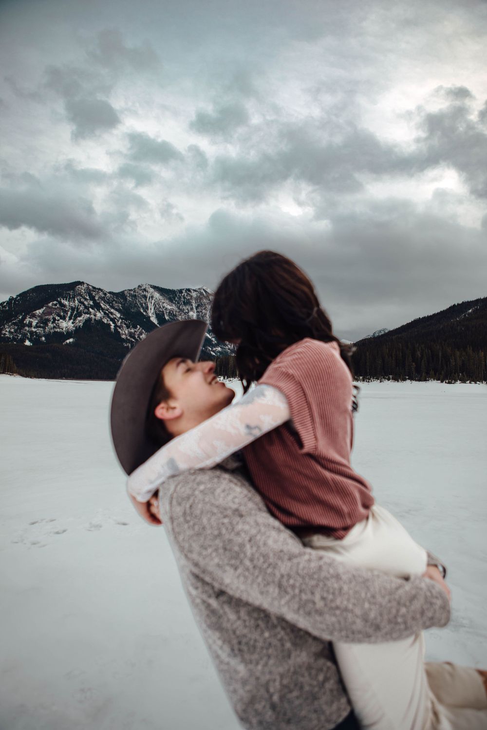 Romantic winter embrace against snowy mountain backdrop with dramatic cloudy sky.