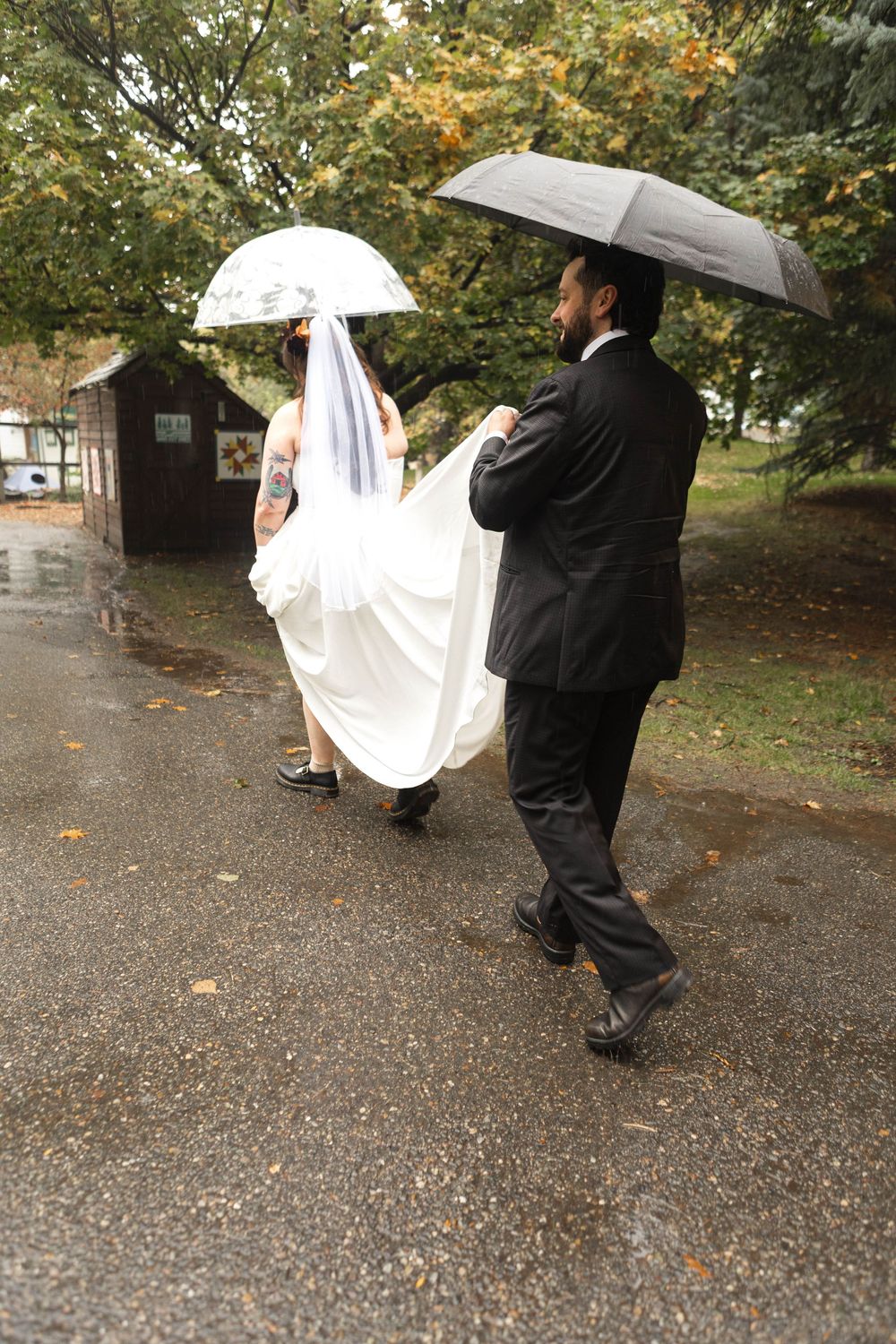 Two people in black and white outfits dance playfully with umbrellas on a rainy autumn path.