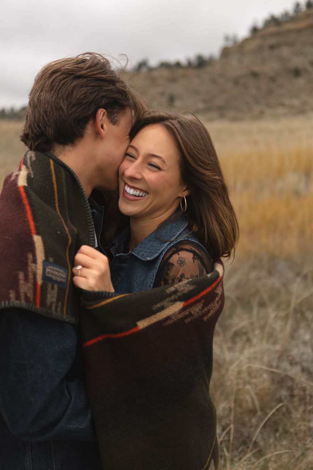 A couple shares joyful embraces and laughter in a golden autumn field at sunset.