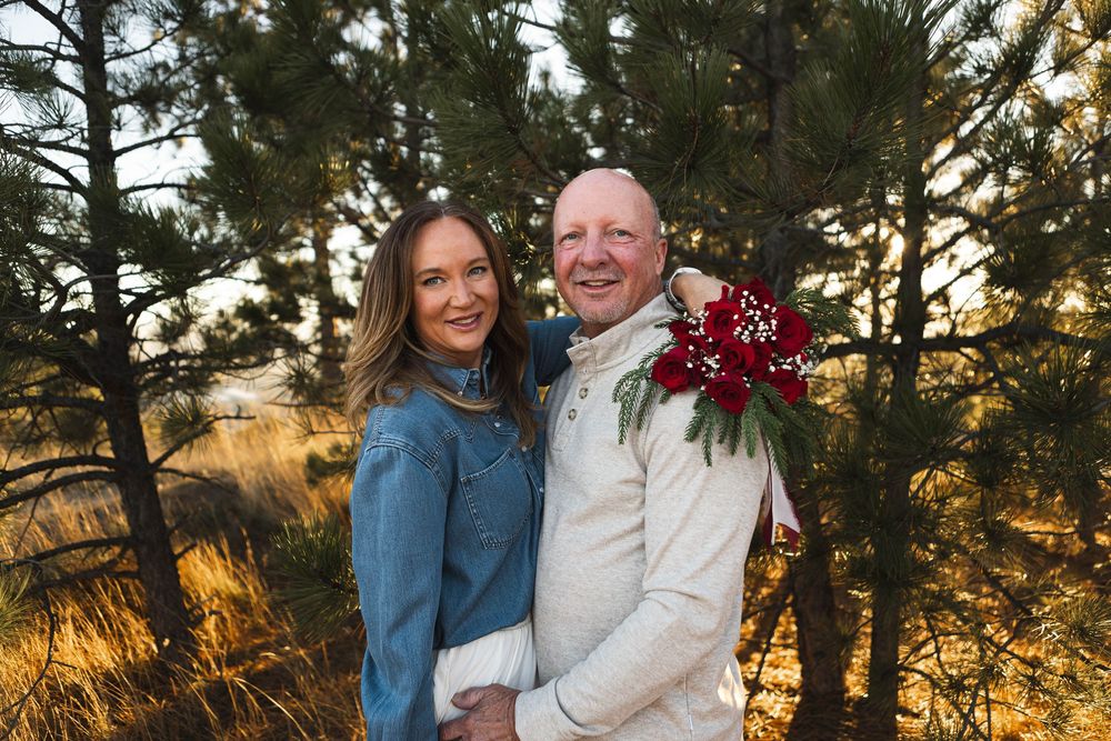 A couple shares a romantic moment among tall pine trees during a golden sunset photo session.