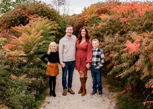 A family poses on a pathway surrounded by vibrant autumn foliage with orange and red colors.