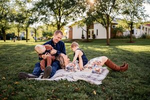 A family relaxes together on a picnic blanket during a warm sunset in a grassy park setting.