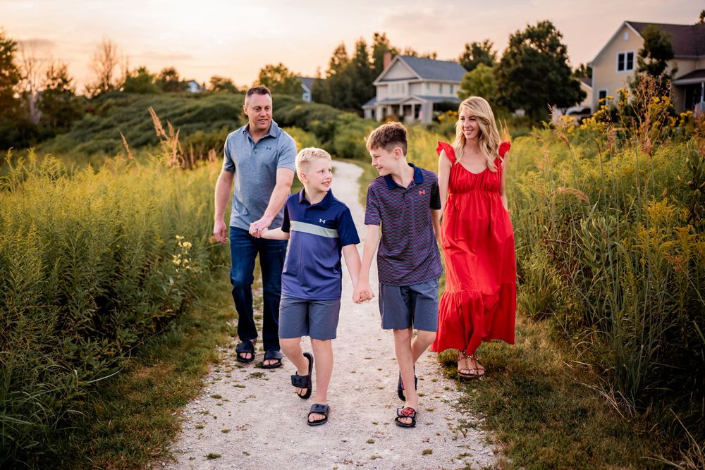 Family walks together on a gravel path through summer meadow at sunset.