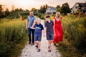 Family walks together on a gravel path through summer meadow at sunset.